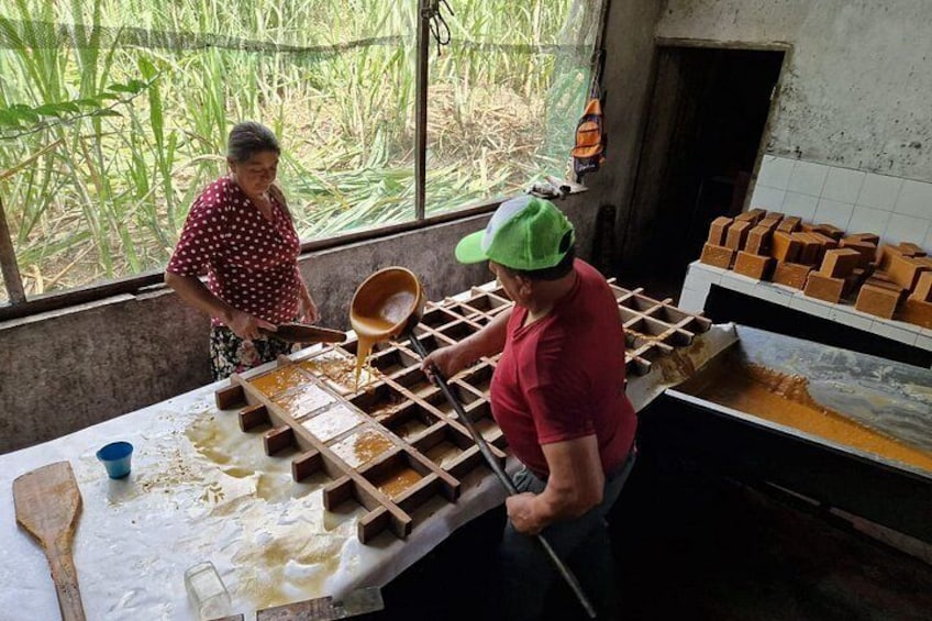 Two people working with a wooden mold and a liquid substance in a rustic kitchen setting. 3
