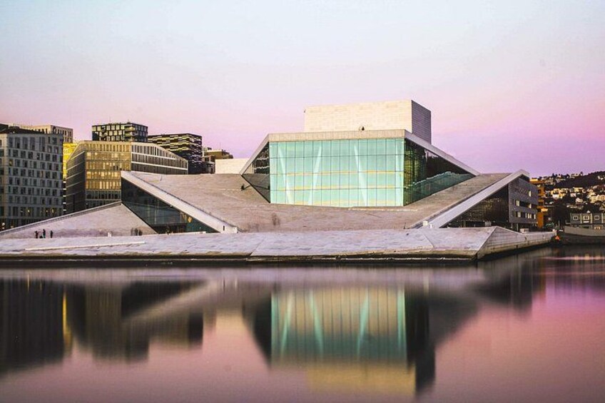A modern building with a glass facade, surrounded by water, and urban buildings in the background. 2
