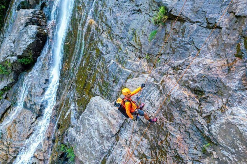 A person rappelling down a rocky cliff with a waterfall in the background. 5