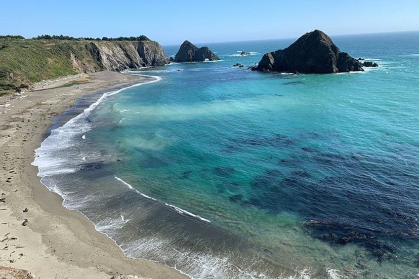 Un paisaje costero con aguas turquesas cristalinas, una playa de arena y afloramientos rocosos. 4