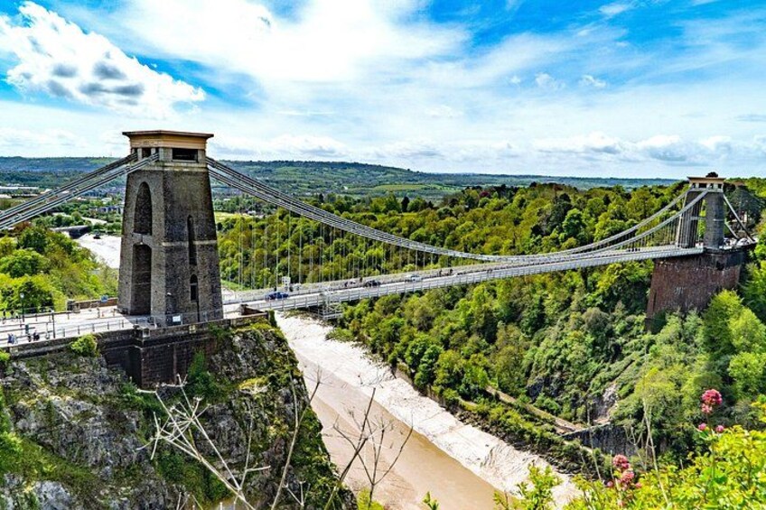 A suspension bridge with towers, a river below, and a forested landscape. 3