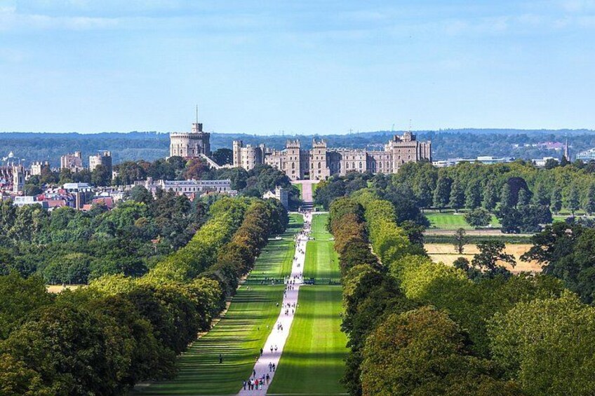 A castle complex with a long, manicured lawn leading to it, surrounded by trees and open fields. 1