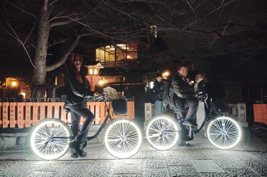 Trois personnes font du vélo sur une piste asphaltée la nuit, leurs roues étant illuminées. 3