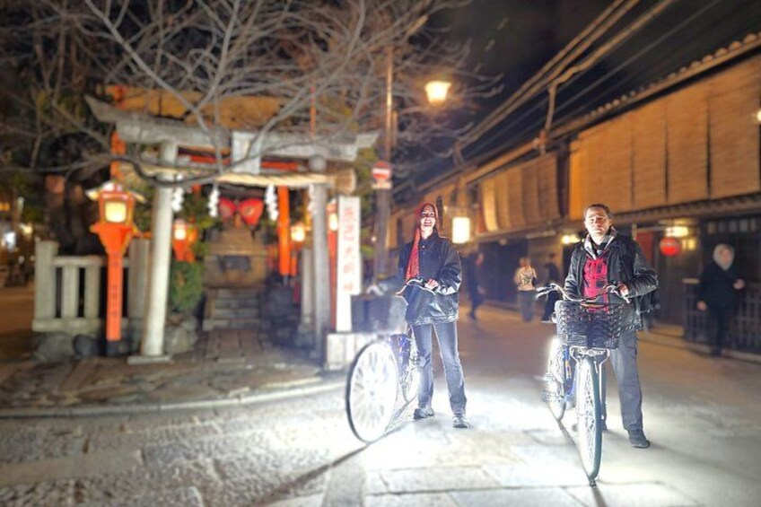 Deux personnes à vélo, une porte torii traditionnelle japonaise et une rue bordée d’immeubles. 2