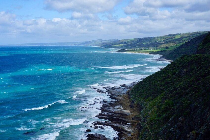 A coastal landscape with a rocky shoreline, ocean waves, and green hills. 5