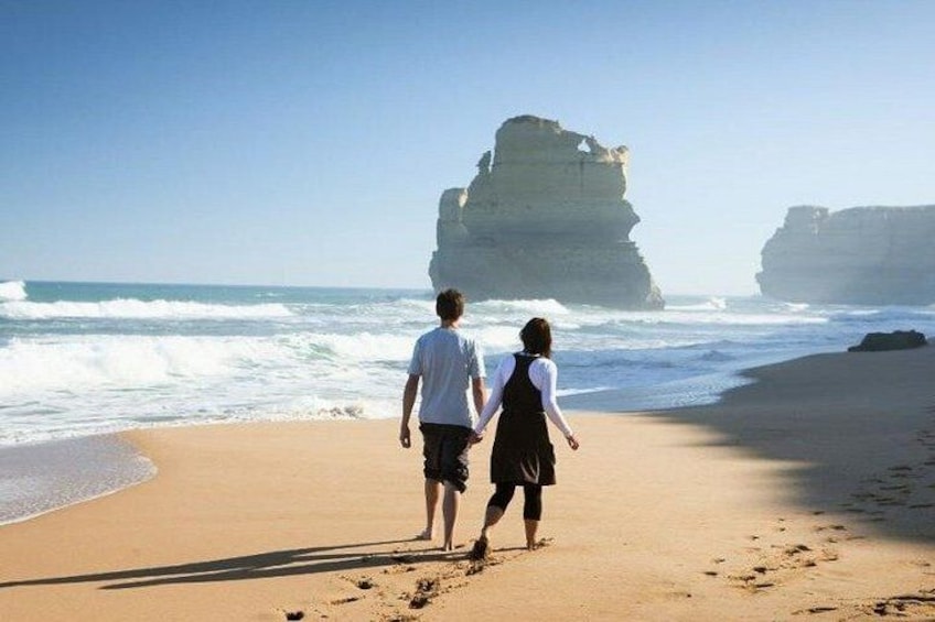 Two people walking on a beach with a large rock formation in the background. 1