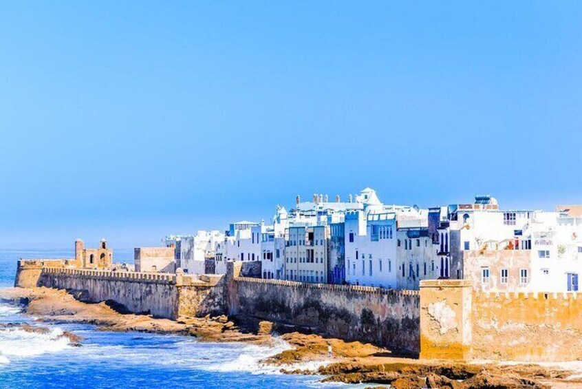 A coastal town with white buildings, a sea wall, and rocky terrain. 5