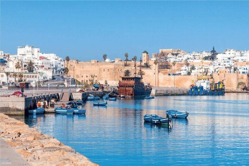 A harbor with boats, a large ship, and a fortified city wall in the background. 1