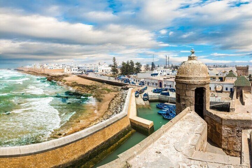 A coastal town with a fortified wall, a small tower, and boats in a harbor. 2