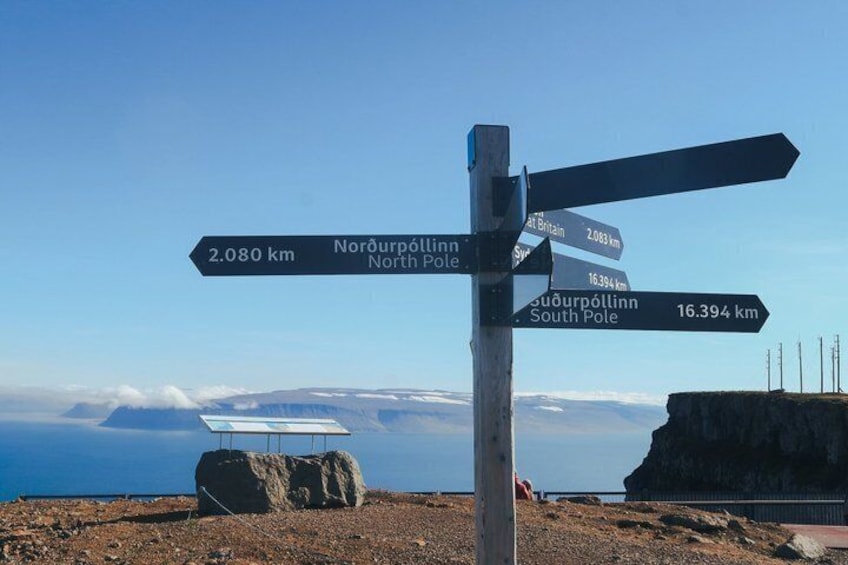 A directional signpost with distances to Norðurlón and Suðurlón, and a view of the ocean and cliffs. 5