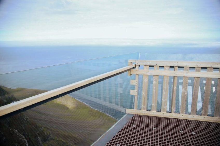 A wooden viewing platform overlooking a coastal landscape with a clear view of the sea and distant land. 4