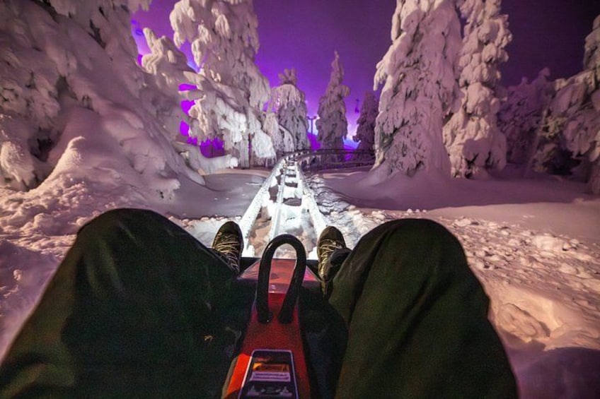 A snow-covered path with trees on either side, a purple sky, and a person lying down with a device in front of them. 3