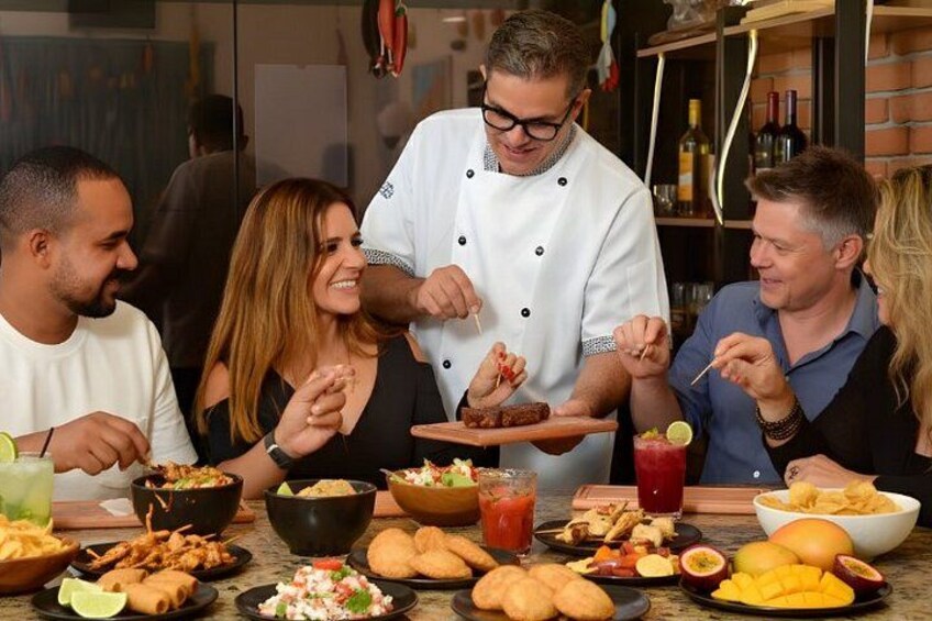 A group of people dining at a table with various dishes, drinks, and a chef serving food. 4