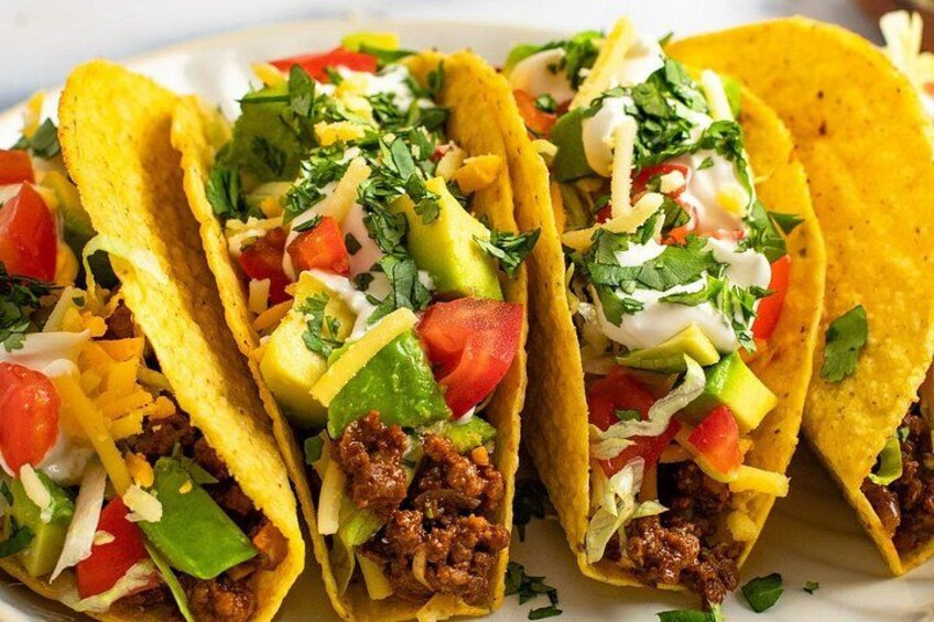 Three tacos with ground meat, cheese, and vegetables on a plate. 2