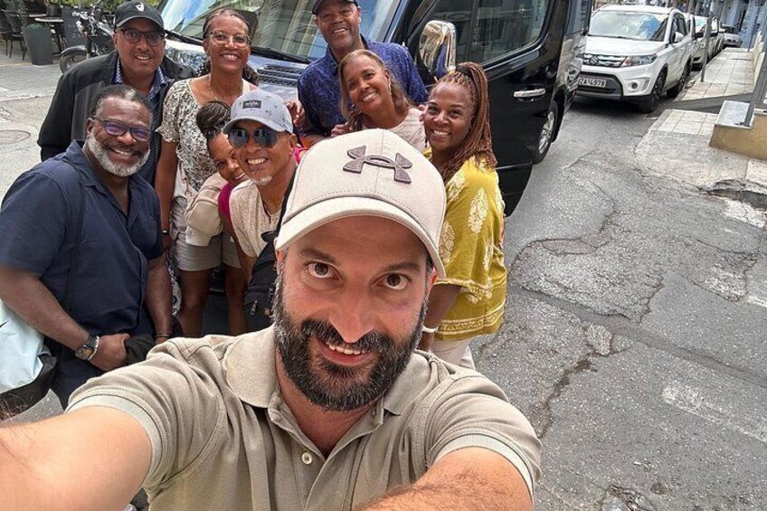 Een groep mensen die een selfie maakt op straat, met geparkeerde auto's en een bus op de achtergrond. 2