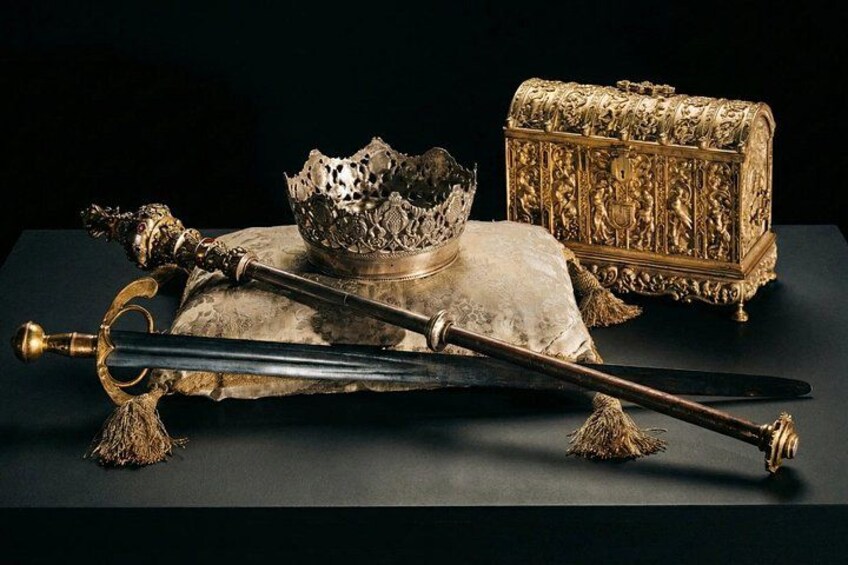 Een verzameling antieke voorwerpen, waaronder een zwaard, een kroon en een decoratieve doos op een donkere ondergrond. 1