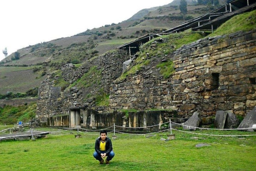 A stone building with a grassy foreground and a hilly background. 1