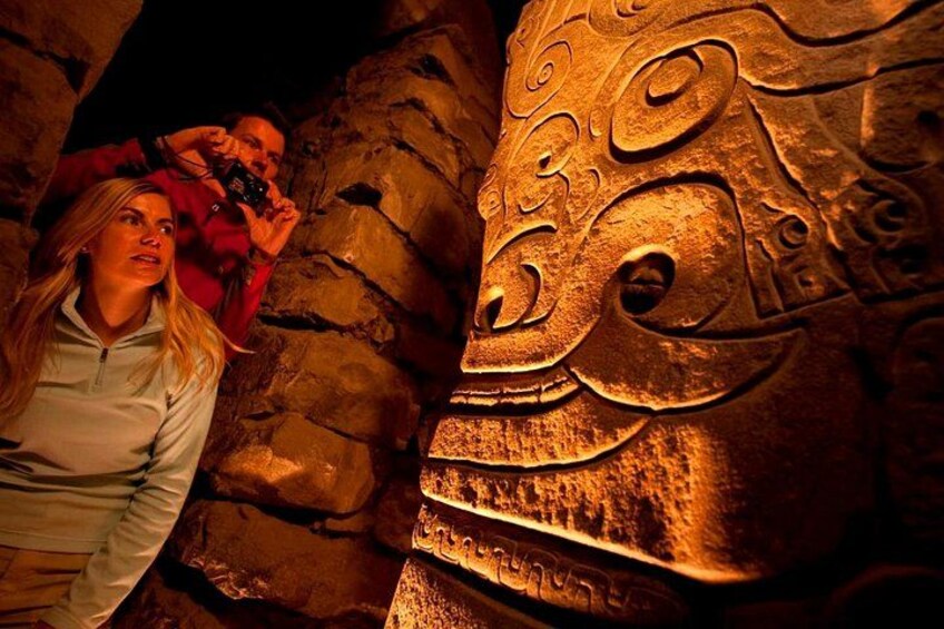 A stone carving with intricate patterns, a person taking a photo, and a cave-like setting. 2