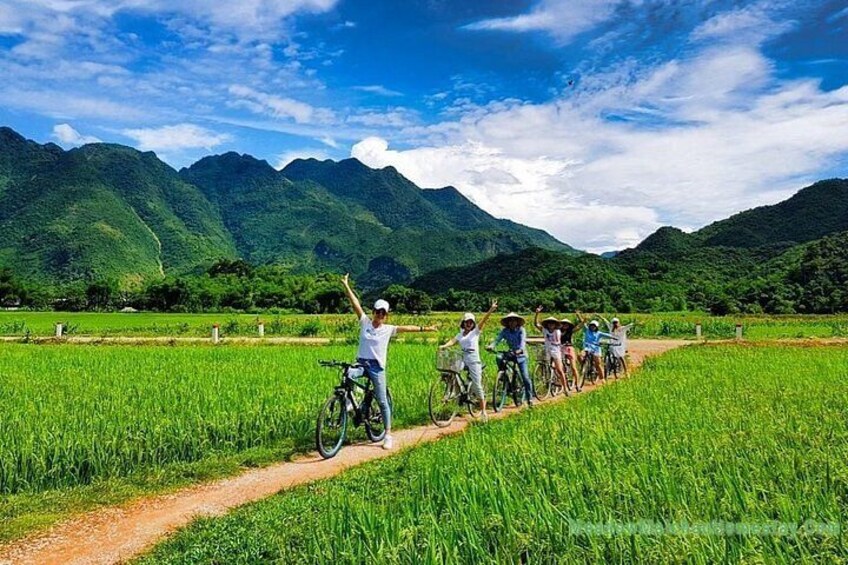 A group of people on bicycles in a green field with mountains in the background. 4