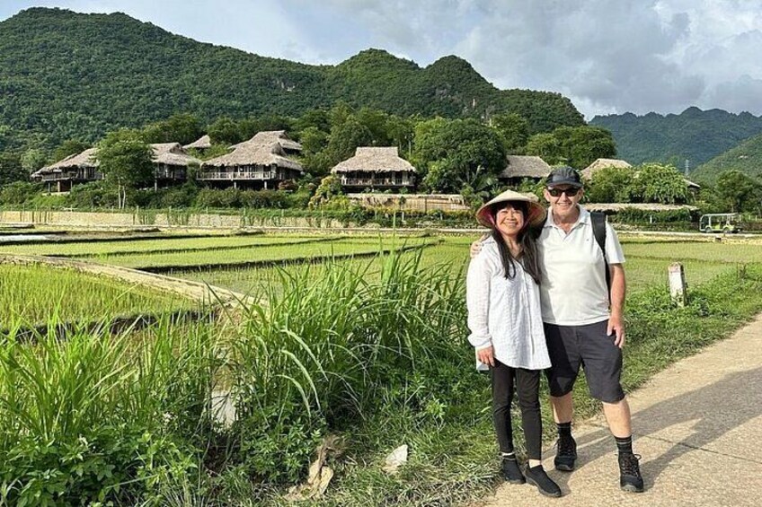 A couple standing in a rice paddy field with traditional houses in the background. 1