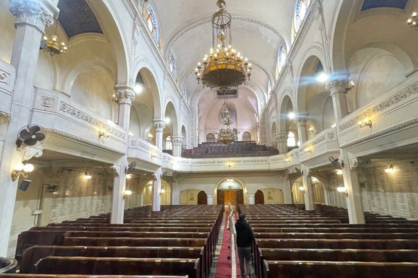 En interiörbild av en stor sal med rader av träbänkar, välvda tak och en stor kristallkrona i mitten. 5