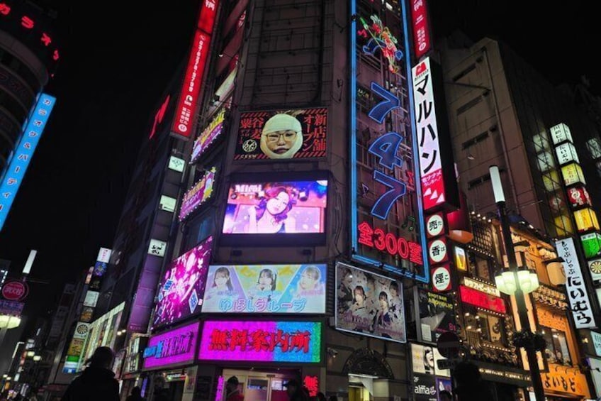 A brightly lit urban street at night with illuminated billboards and signs. 4