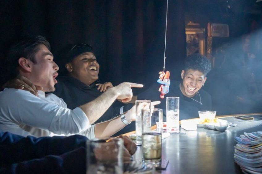 Three people at a bar with drinks and a hanging toy. 1