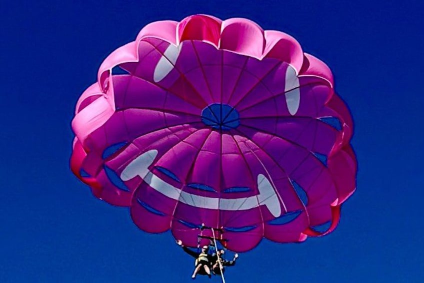 A person parachuting with a large, colorful parachute against a clear blue sky. 3