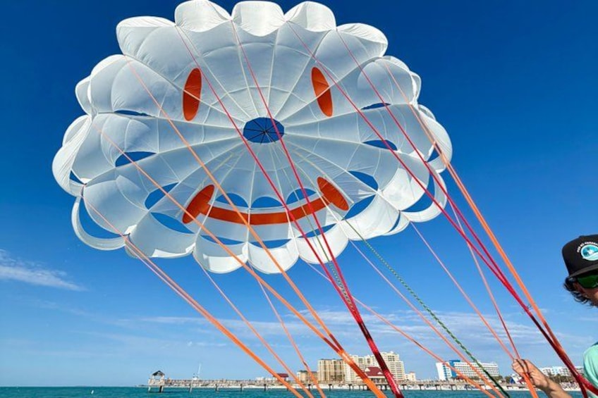 A parachute with multiple compartments and red and blue lines, over a coastal cityscape with buildings and a pier. 2