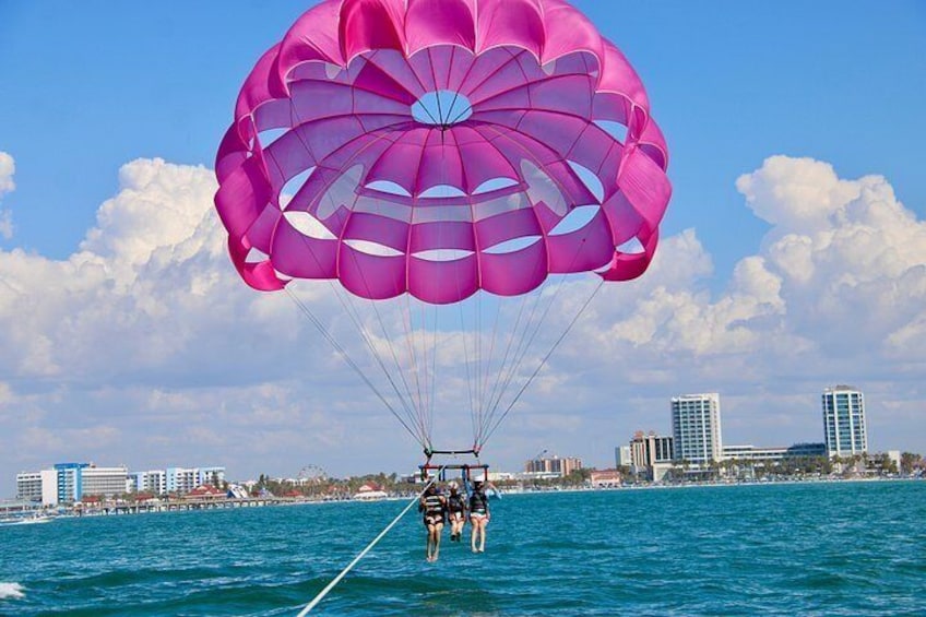 A parasailing activity with a pink parachute over the water, a city skyline in the background, and a clear sky. 3