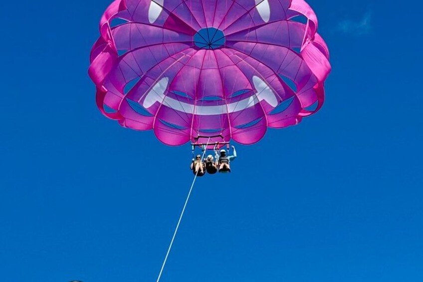 A parachute with a person and a small object attached to it, suspended in the air against a clear blue sky. 5