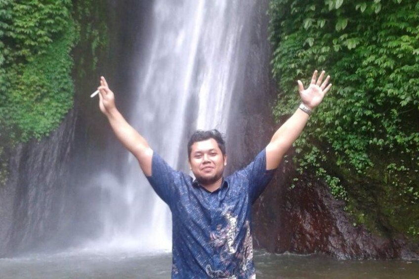 Una persona de pie frente a una cascada, con los brazos levantados. 2