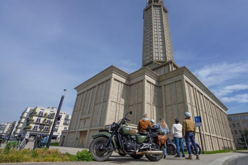 Un edificio grande con una torre alta, una motocicleta y un grupo de personas de pie cerca. 2