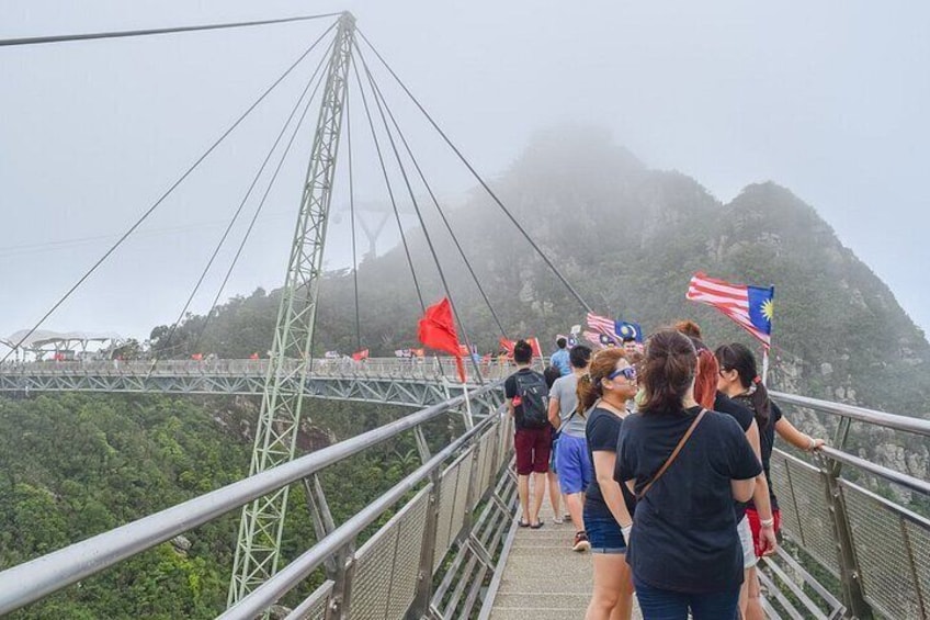 A suspension bridge with people walking on it, flags, and a mountainous landscape in the background. 2