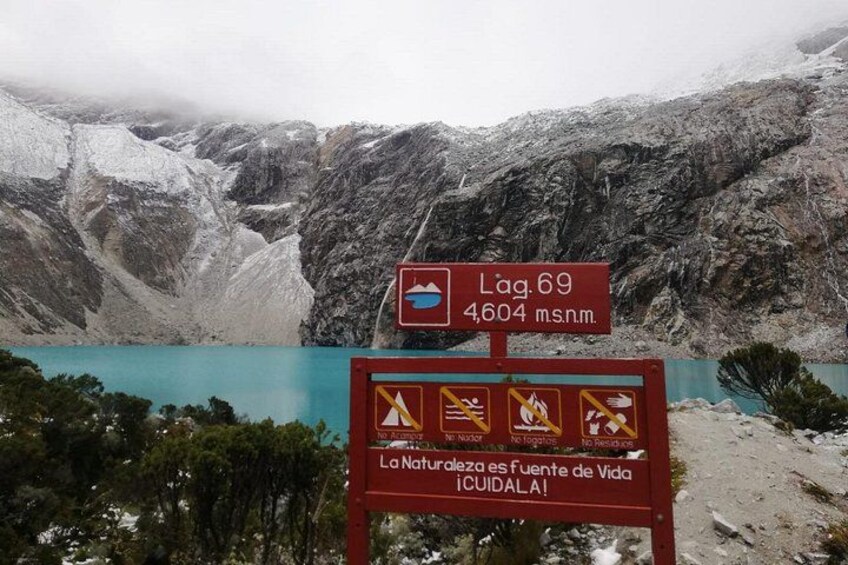 A mountainous landscape with a lake, a sign indicating Lag.69 at 4604 meters, and a warning sign about natural hazards. 3