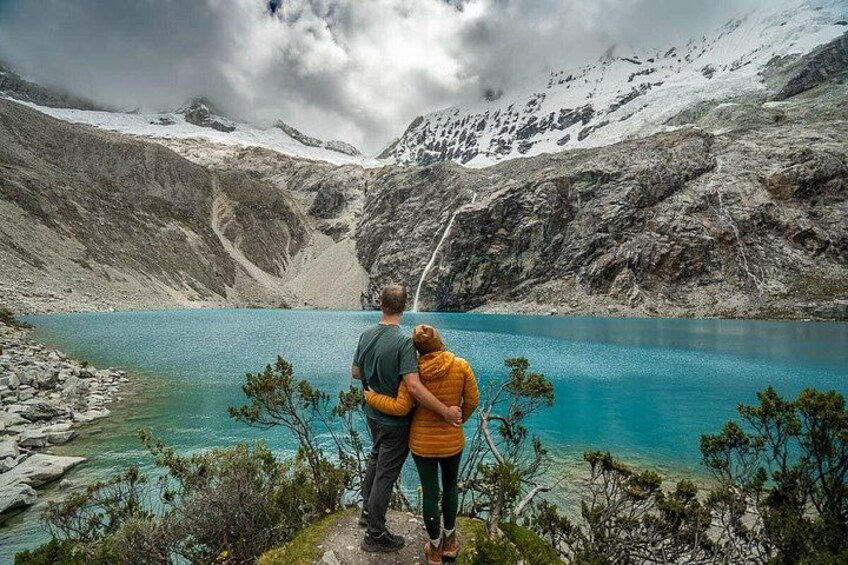 A couple standing by a turquoise lake with mountains in the background. 5
