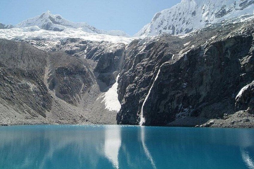 A glacier with a waterfall, a clear blue lake, and snow-covered mountains. 2