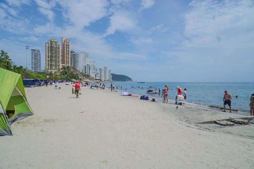 A beach with people, tents, and high-rise buildings in the background. 3