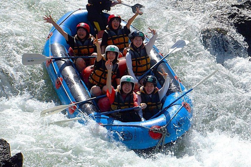 A group of people in a blue inflatable raft navigating through white water rapids. 1