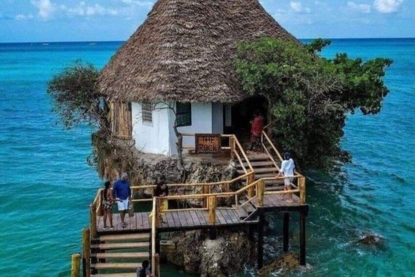 A thatched-roof hut on a wooden pier over turquoise water. 1