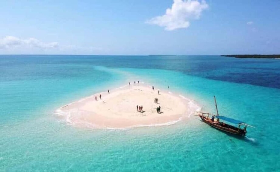 A small island with people and a boat in clear turquoise waters. 5
