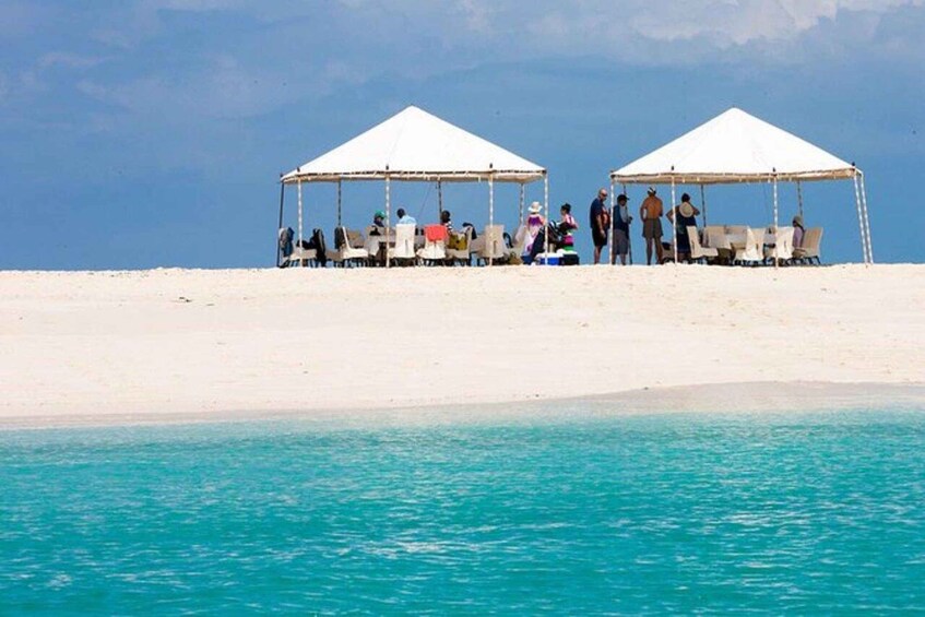 Two white tents on a sandy beach with turquoise water in the foreground. 2
