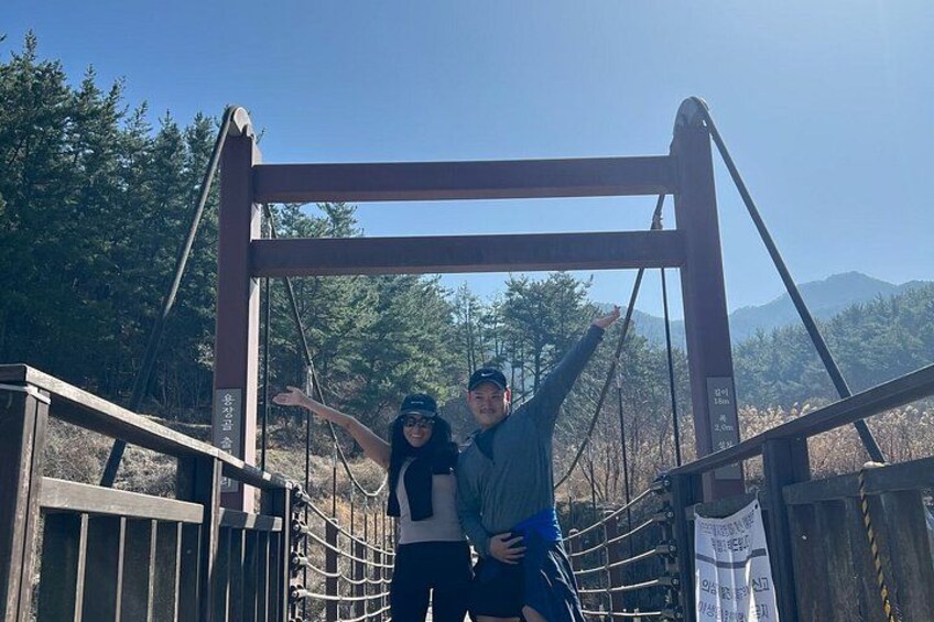 A wooden bridge with metal supports, surrounded by trees and mountains in the background. 2