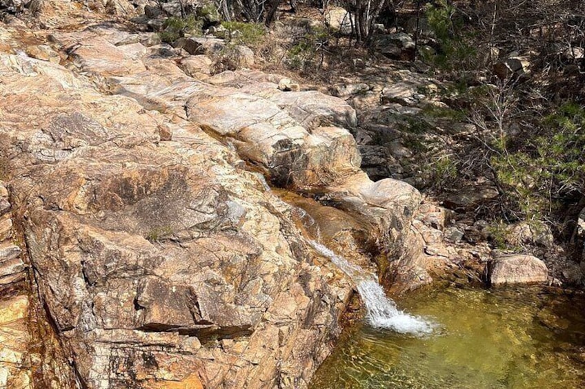 Een rotsachtig landschap met een kleine waterval en een helder stroompje aan de voet ervan. 2
