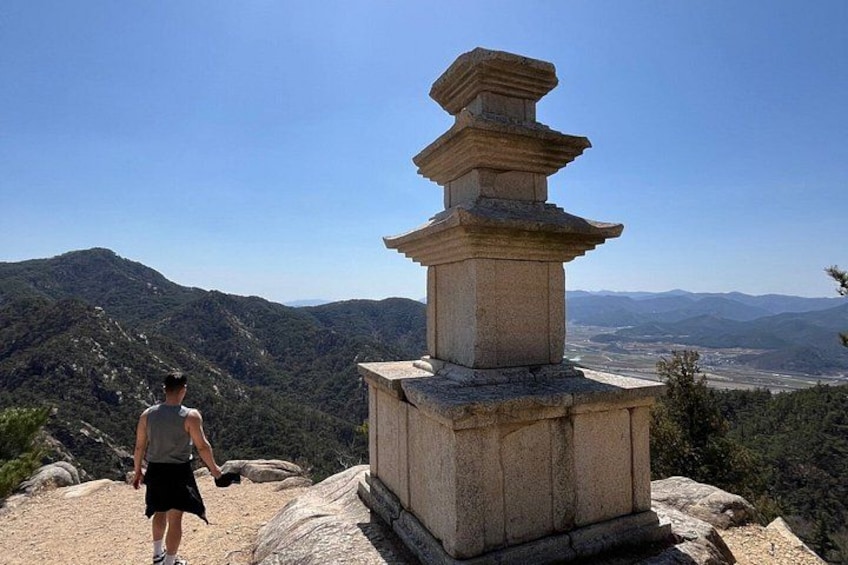 A person standing near a stone pagoda with a mountainous landscape in the background. 1