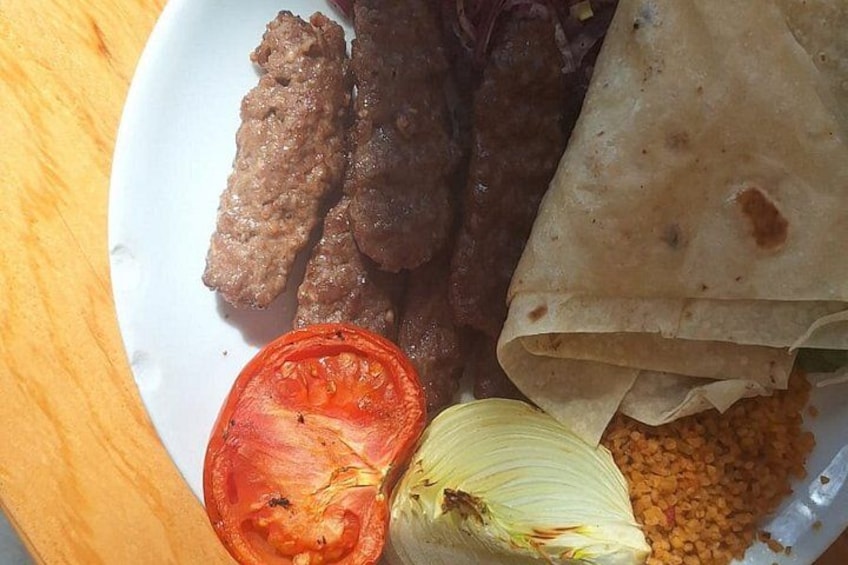 Une assiette avec des brochettes de viande, une tranche de tomate, un oignon et une galette. 4