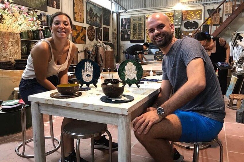 Two people seated at a table with pottery and decorative items in a workshop. 5