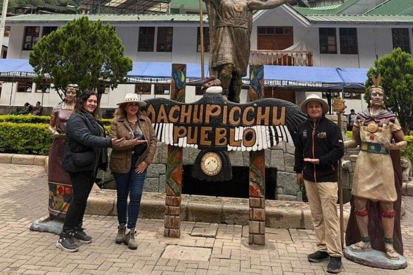 A group of people standing in front of a statue with a sign that reads 'Machupicchu Pueblo.' 4