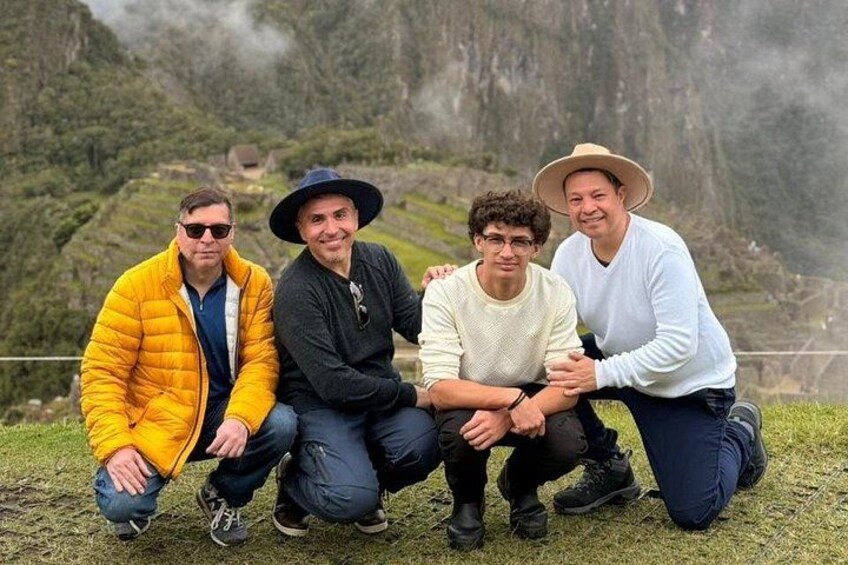Four people sitting on grass with a mountainous landscape in the background. 3