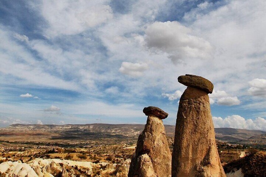 Two stone monoliths in a barren landscape with a distant view of hills and a cloudy sky. 4